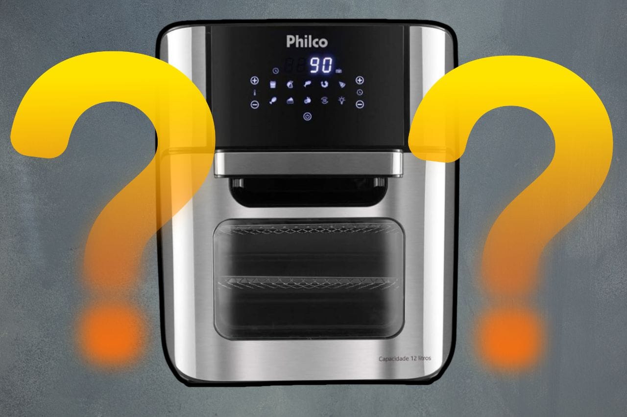Uma air fryer oven da Philco preta com detalhes em inox em uma cozinha, ao lado de alguns legumes frescos.